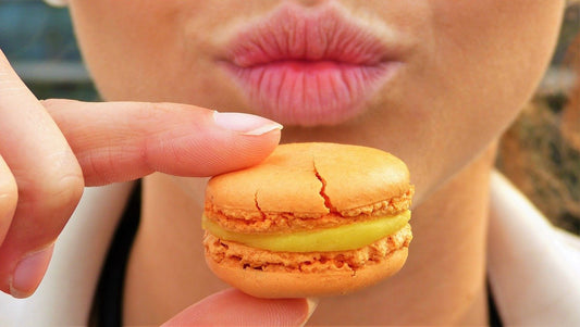 Main tenant un macaron entre les doigt avec une bouche en arrière plan