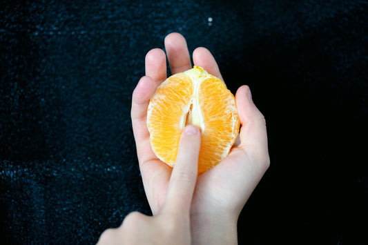 Une demi orange pausé sur une main et le doigt de l'autre main touche l'intérieur de l'orange